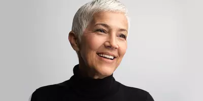 Mujer adulta con el pelo corto y blanco, sonriendo con un suéter negro de cuello alto