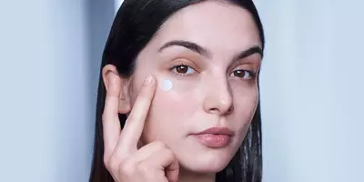 Una mujer que se aplica la crema hidratante para ojos Génifique de Lancôme sobre la piel seca alrededor de los ojos
