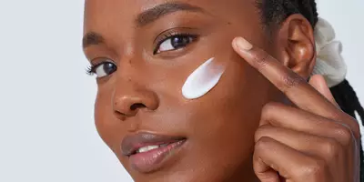 Mujer aplicando uno de los mejores humectantes de Lancôme para piel seca en la mejilla