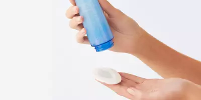 Mujer que muestra cuánto desmaquillador debe dispensar en una almohadilla de algodón