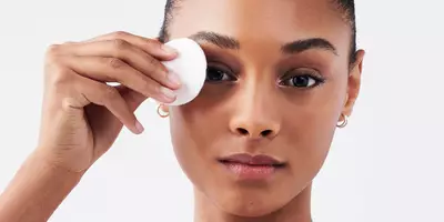 Mujer con piel oscura quitando maquillaje de ojos con una almohadilla redonda de algodón y un removedor de maquillaje de ojos bifacil