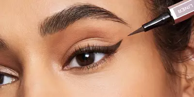 Mujer aplicando delineador líquido marrón en forma de delineador de ojos con alas