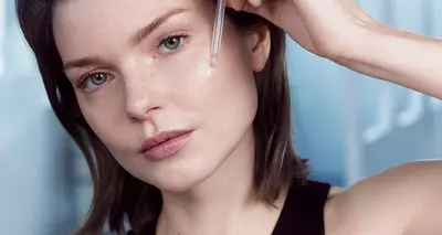 Mujer aplicando el suero facial Advanced Génifique con un gotero