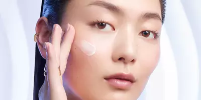 Mujer asiática aplicando crema humectante en la mejilla