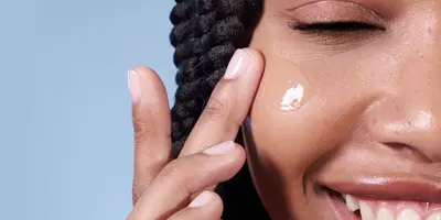 Mujer sonriendo mientras aplica suero hidratante sobre la piel seca del invierno