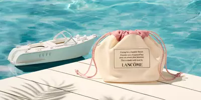 Portacosméticos color canela en un muelle con artículos de tocador de tamaño de viaje de Lancome con una lancha de juguete en el agua