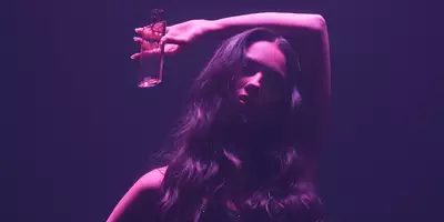 Olivia Rodrigo con cabello largo y holgado bajo luz rosa que sostiene Idole Power eau de parfum Intense