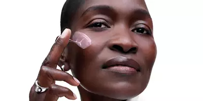 Mujer madura con un tono de piel profundo que aplica la crema de colágeno Renergie, parte de la rutina que favorece el colágeno